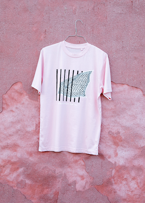 A pink T-shirt with a black and white abstract design hangs on a metal hanger against a textured pink wall.