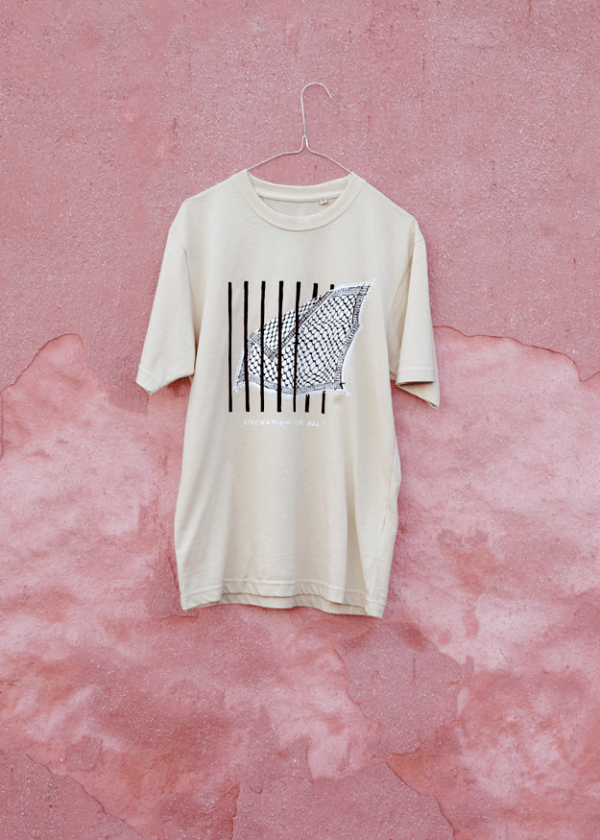 A beige T-shirt with a black and white abstract design hangs on a wire hanger against a textured pink wall.