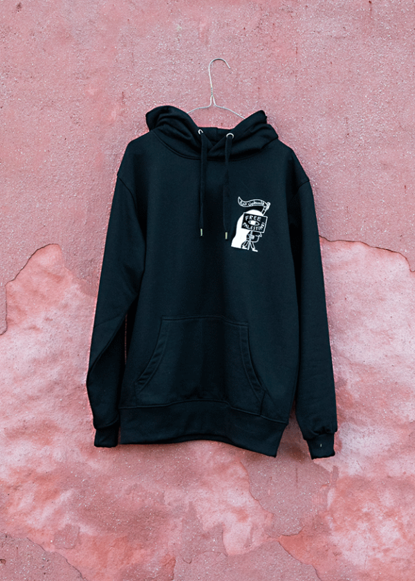 A black hoodie with a printed design on the chest hangs on a hanger against a textured pink wall.